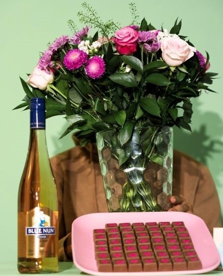 זר פרחים ורוד, שוקולדים ויין על רקע ירוק