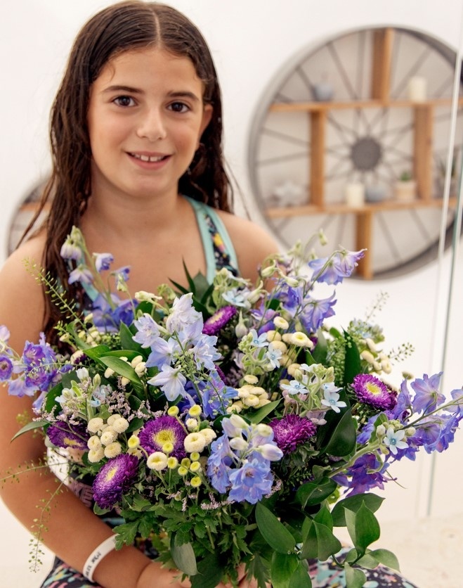 ילדה מחזיקה זר פרחים כחולים וסגולים ומחייכת