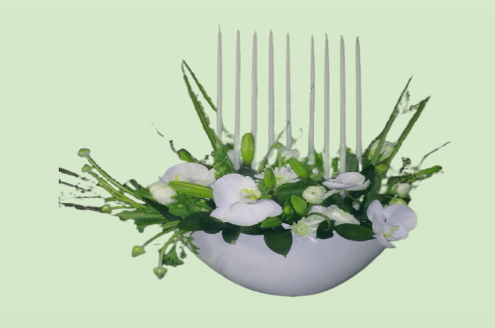 חנוכייה ונרות לבנים מוקפים בפרחים לבנים וירוקים